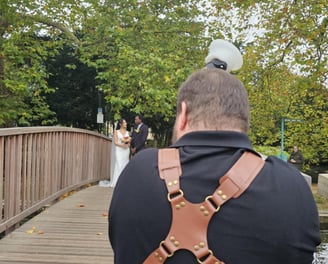 A Hertfordshire bride & groom standing on a wooden bridge over a river, the bridge is sorrounded by trees in autumnal colour 