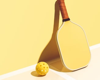 Minimalist yellow pickleball paddle and ball on a bright court, representing Smart Dinker’s sport