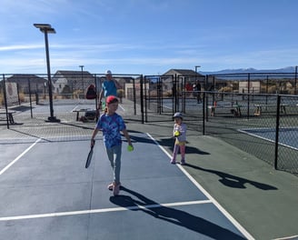 Kids and coach playing pickleball on outdoor courts, promoting family-friendly Smart Dinker training