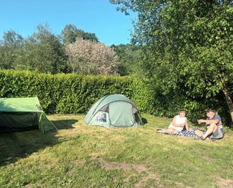 Two people relaxing on the grass beside a tent on a grassy pitch at Les Vieilles Forges campsite in 