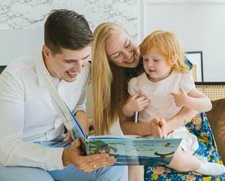 A mother and father reading a children's picture book to a child.