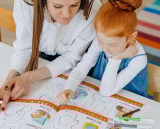 A young girl reading a children's picture book with a teacher.