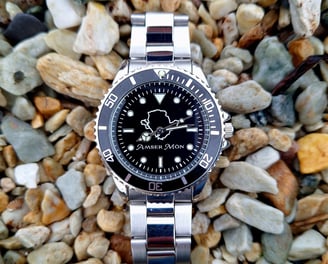 Amser Mon Anglesey black and white metal watch on pebbles on a beach