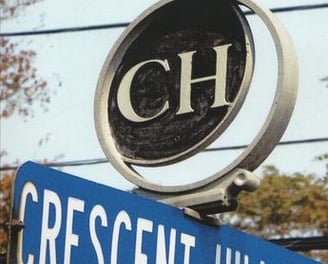 A Street sign of Crescent Hills Rd showing a logo mounted on top with the letters C H