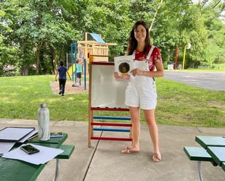 Young woman holding a children's book for a reading in the park event at Crescent Hills park