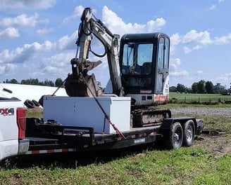 A flatbed trailer hauling a mini excavator 