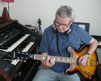 photograph of Julian Sumner with guitar and keyboards in recording studio