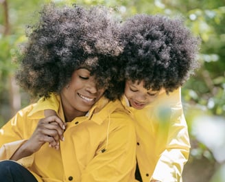 a woman and a young child wearing yellow rain jackets sitting on a bench smiling together