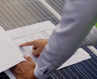 um homem de camisa social apontando um desenho técnico sobre um módulo fotovoltaico