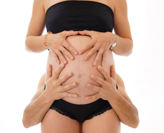 Photo de grossesse avec les mains des futurs parents posées sur le ventre bien rond