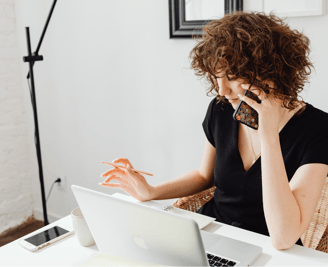 a woman sitting at a table with a laptop and a mobile phone