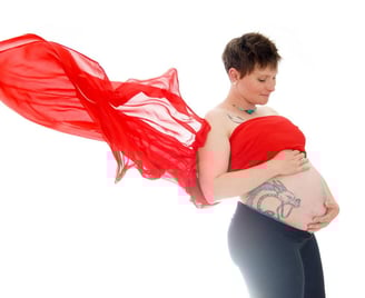 Photo de grossesse avec un voile volant rouge et la future mère tenant son ventre