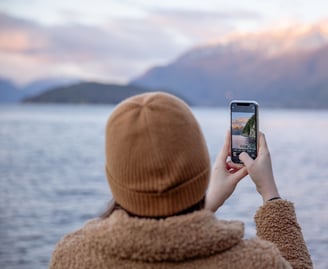 Alleine reisende Frau mit Smartphone am See fotografiert die Landschaft