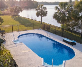 a pool with a fenced in area with a bench and chairs