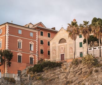 Palm trees - faded frescoed church - terracotta-hued buildings on rocky hillside - Bogliasco