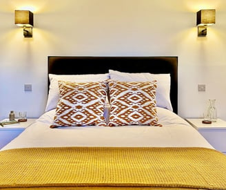 a large bed with wall lights and colourful cushions and throw