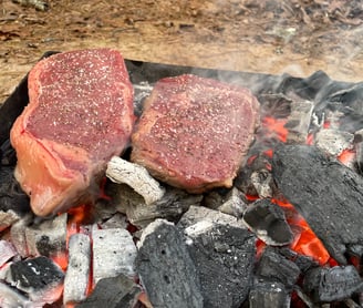 Ribeye and new york strip steaks over a live bed of lump charcoal