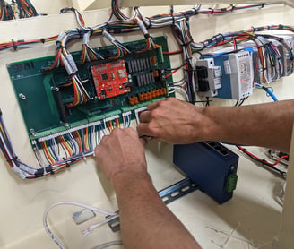 two hands holding a wiring harness with a rainbow of wires leading to a green circuit board