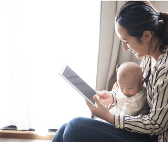 Madre sentada  con un bebe de pocos meses en brazos viendo una tablet
