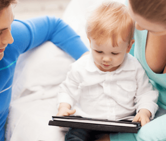 Pareja de padres jóvenes que esán con  un niño de dos años viendo una tablet.