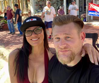 woman with her arm over mans shoulder smiling and taking a photo