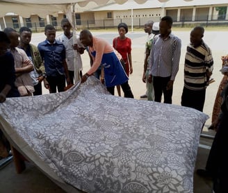 a group of people standing around a bed with a blanket