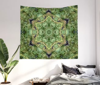 Tapestry on wall with bed underneath and a plant to the left of the bed