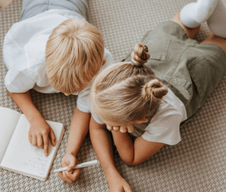 two kids laying on floor and writing