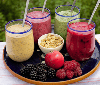 four smoothie glasses in tray with some fruits