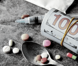 a spoon has tablets and a syringe and a bundle of cash