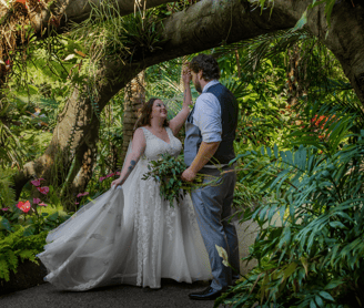 a bride and groom standing in a lush green tropical garden at the Calgary zoo
