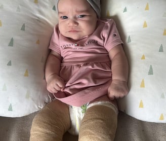 a baby girl in a pink outfit is sitting on a pillow
