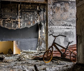 Estancia de una vivienda después de un incendio, se ve bicicleta quemada, paredes y muebles quemados