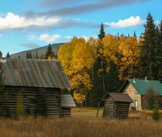 a log cabin in the woods with a blue sky and clouds