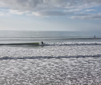 A surfer trimming along a clean peeling wave at Ynyslas, calm seas and blue skies.