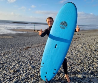 A smiling surfer holding a light blue Alder Glide surf board with two thumbs up