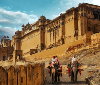 two people riding on elephants in front of a castle Amber Palace top 5 tourist places in India rajas