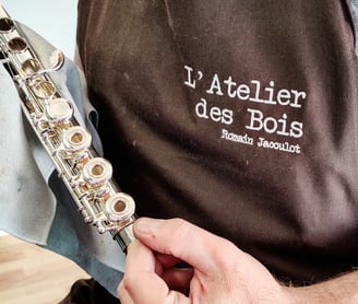 une vue de près du réparateur Romain Jacoulot avec son tablier de travail, tenant une flûte