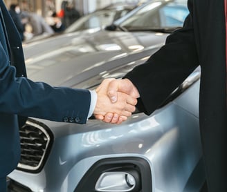 un hombre y una mujer se dan la mano delante de un coche