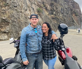 man with his arm around a woman with two motorcycles behind them