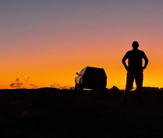 a man standing in the sunset with a car in the background