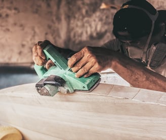 Craftsman shaping a handmade balsa surfboard with an electric planer