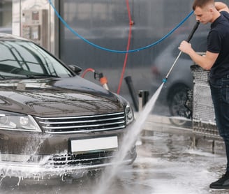 um homem lavando um carro com bico de lavadora a pressão