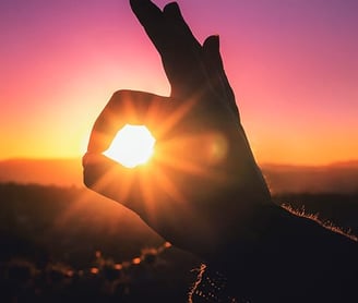 a person holding up a peace sign with the sun setting in the background