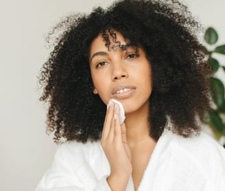 A woman in a robe holding up a face cotton pad