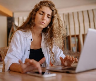 A stressed woman using a calculator and a laptop