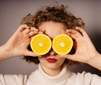Woman holding up 2 orange slices to her face to cover her eyes.