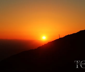 a sunset on a hill with a cross on the top of a hill