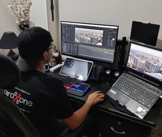 a man sitting at a desk with a laptop and a laptop editing drone video of aeroxone compnay 