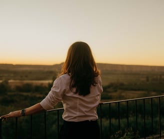 a woman standing on a balcony with a view of the sunset